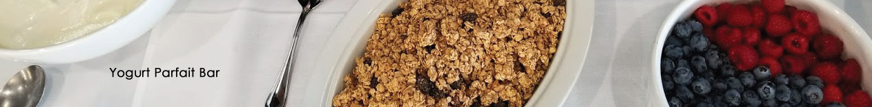 Yogurt Parfait Bar, pic with granola, raspberries, blueberries, and yogurt in bowls on a white tablecloth with spoon.