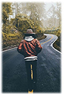 Start Here path visual, man walking down winding road with hands in his pockets, back to us, has on a tan hat and red jacket, black pants.