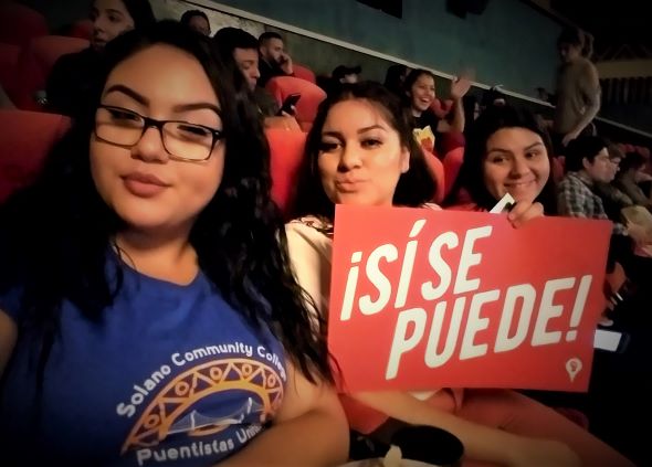 Three Puentistas Listening to Dolores Huerta holding a sign that says si se puede.
