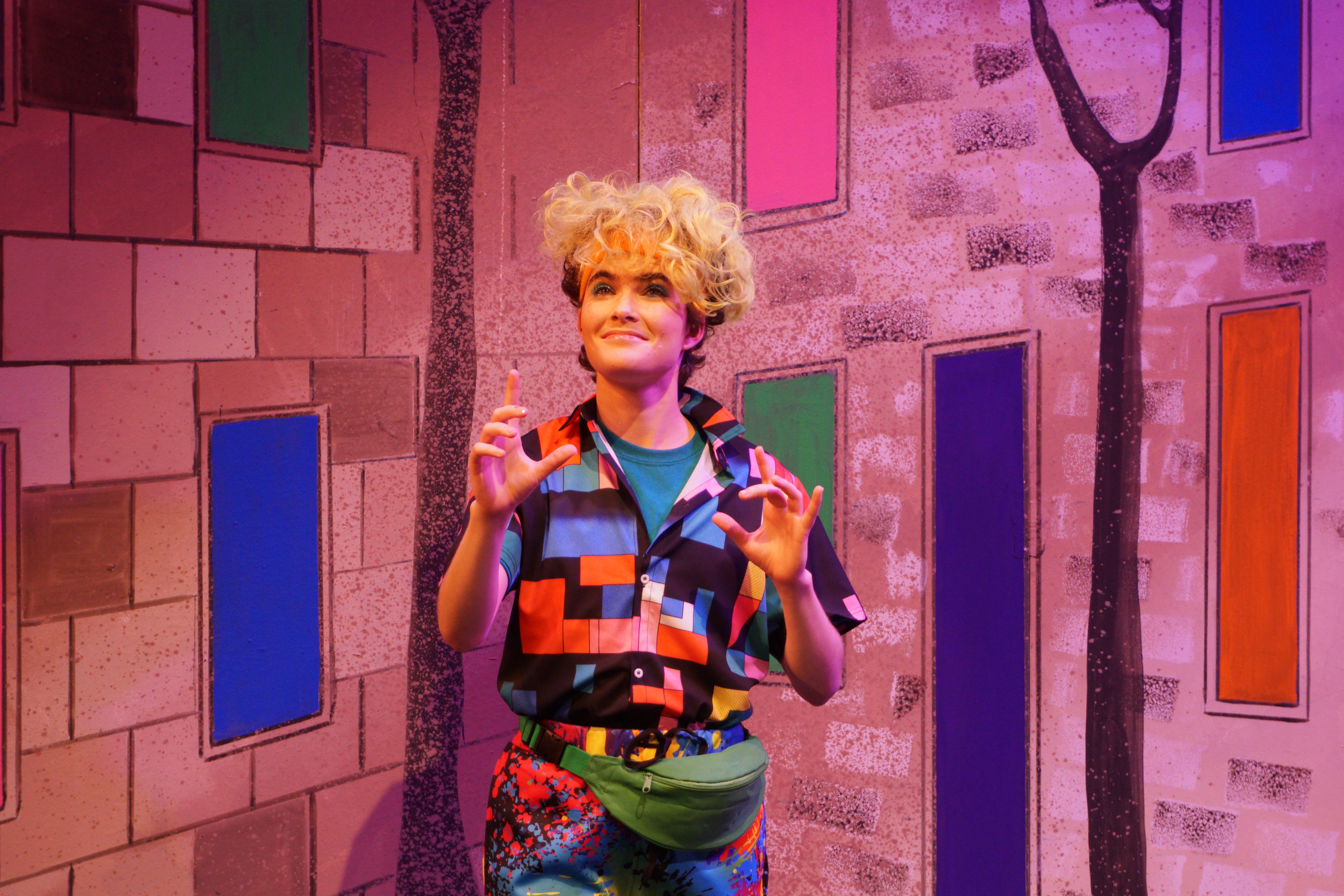 A person in front of a set wearing multi colored clothing from the 80s
